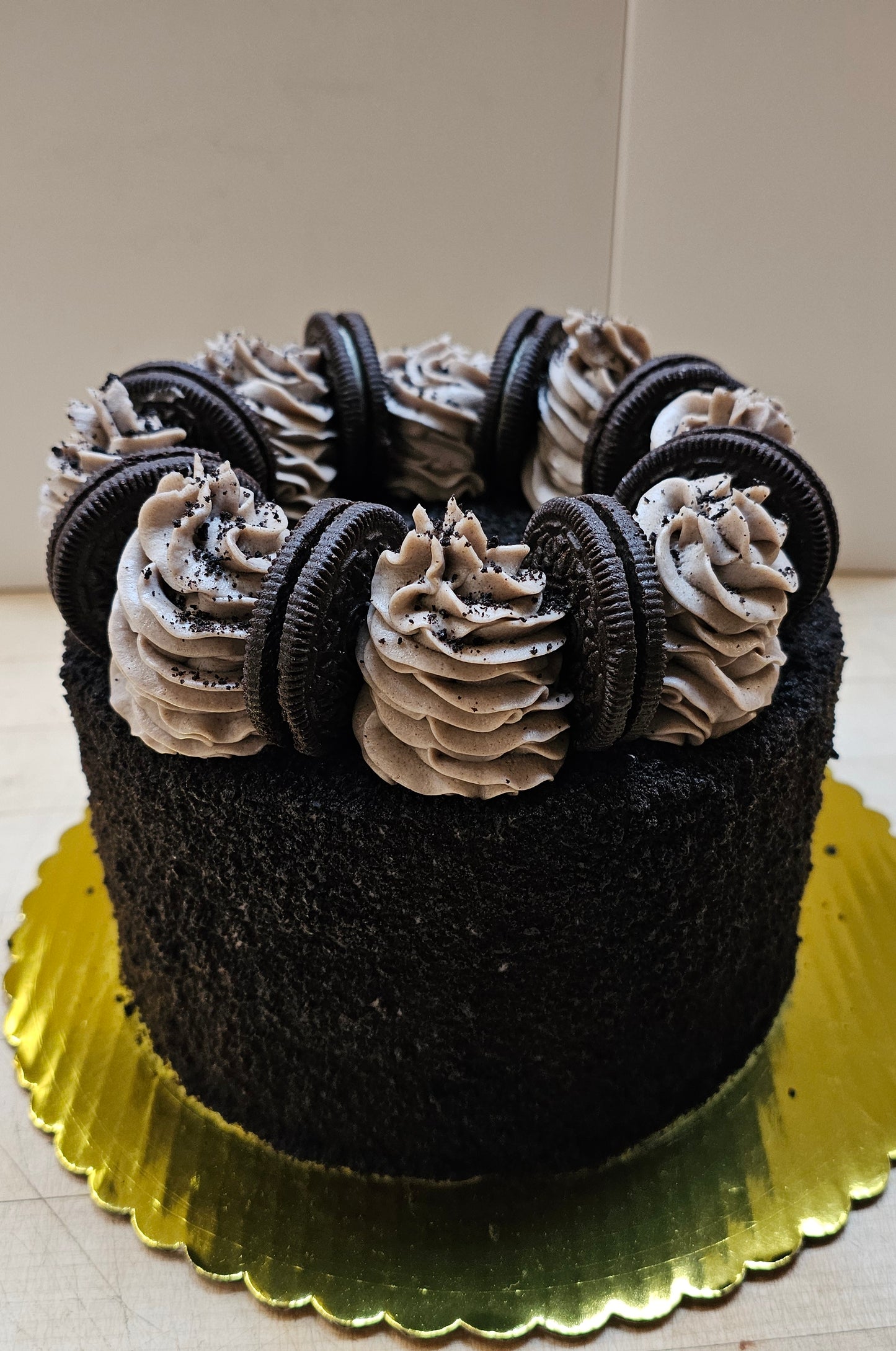 An Oreo cake covered in Oreo colored cake crumbs, topped with whole Oreos and spirals of frosting.