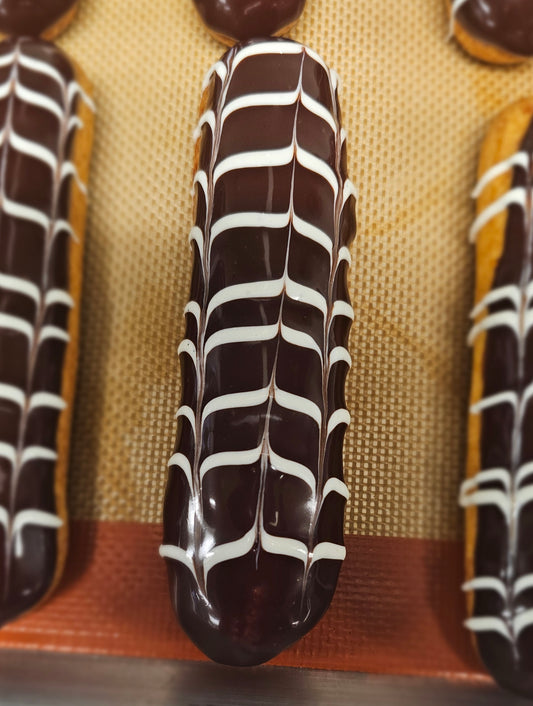 An eclairs with dark chocolate glaze and white horizontal lines.