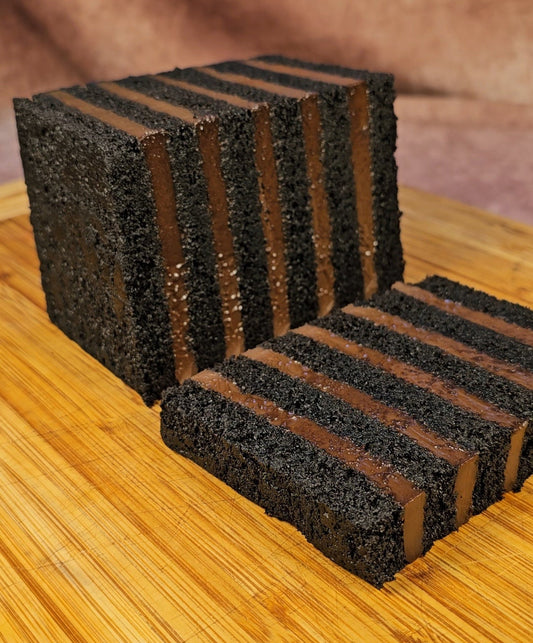 A rectangular dark chocolate layer cake with alternating dark chocolate cremeux layers, shown sliced and standing on a wooden board against a warm brown background.