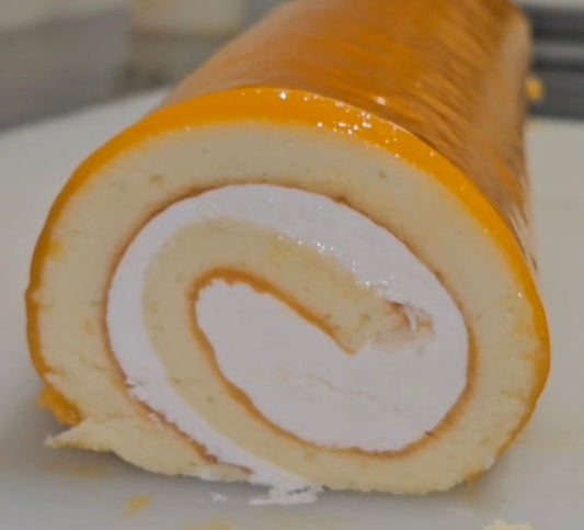 Sliced edge of a Swiss roll cake with white cream filling and orange glaze on a white surface.