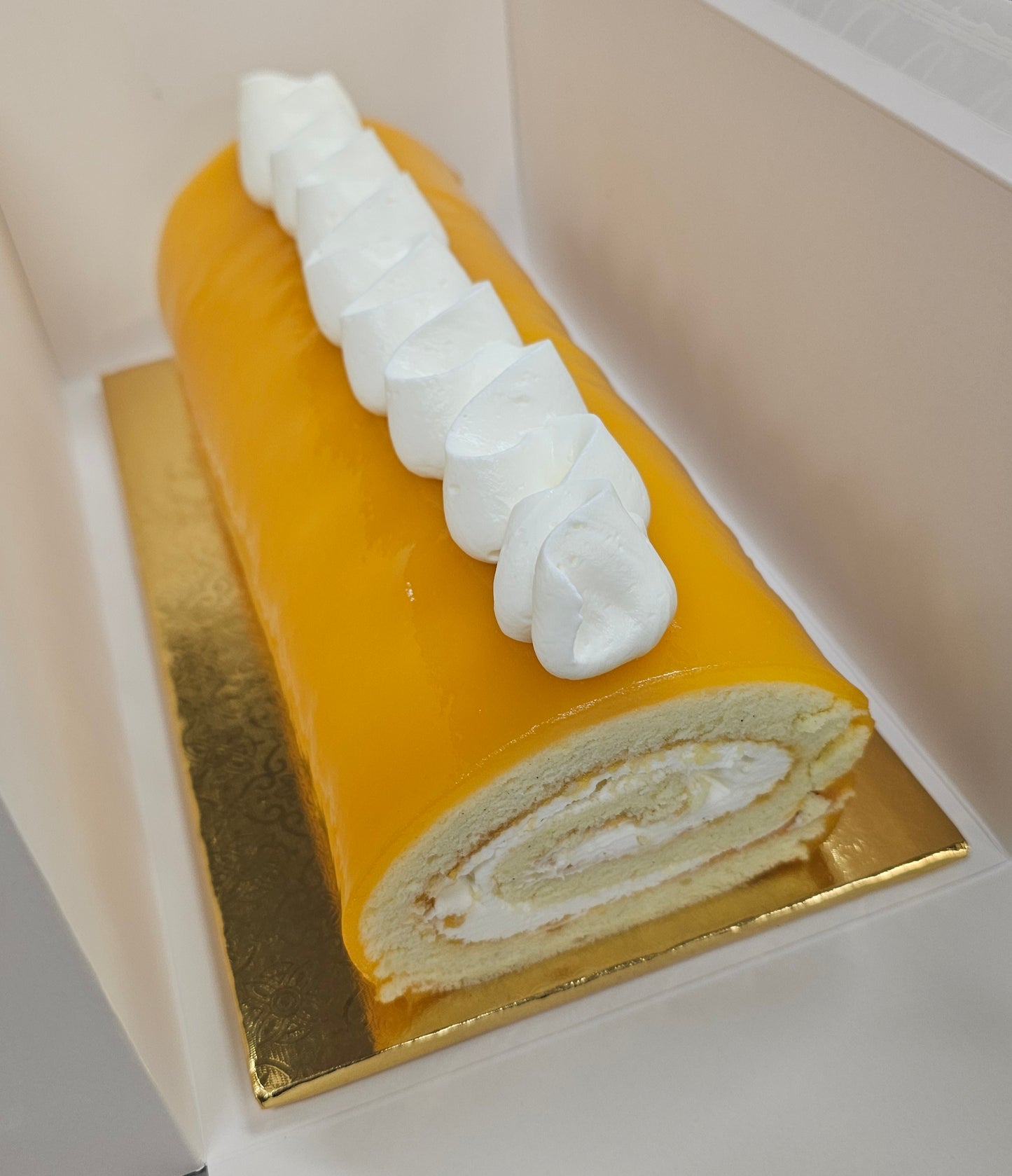 Mango Roll cake with white cream on top, placed on a gold base.