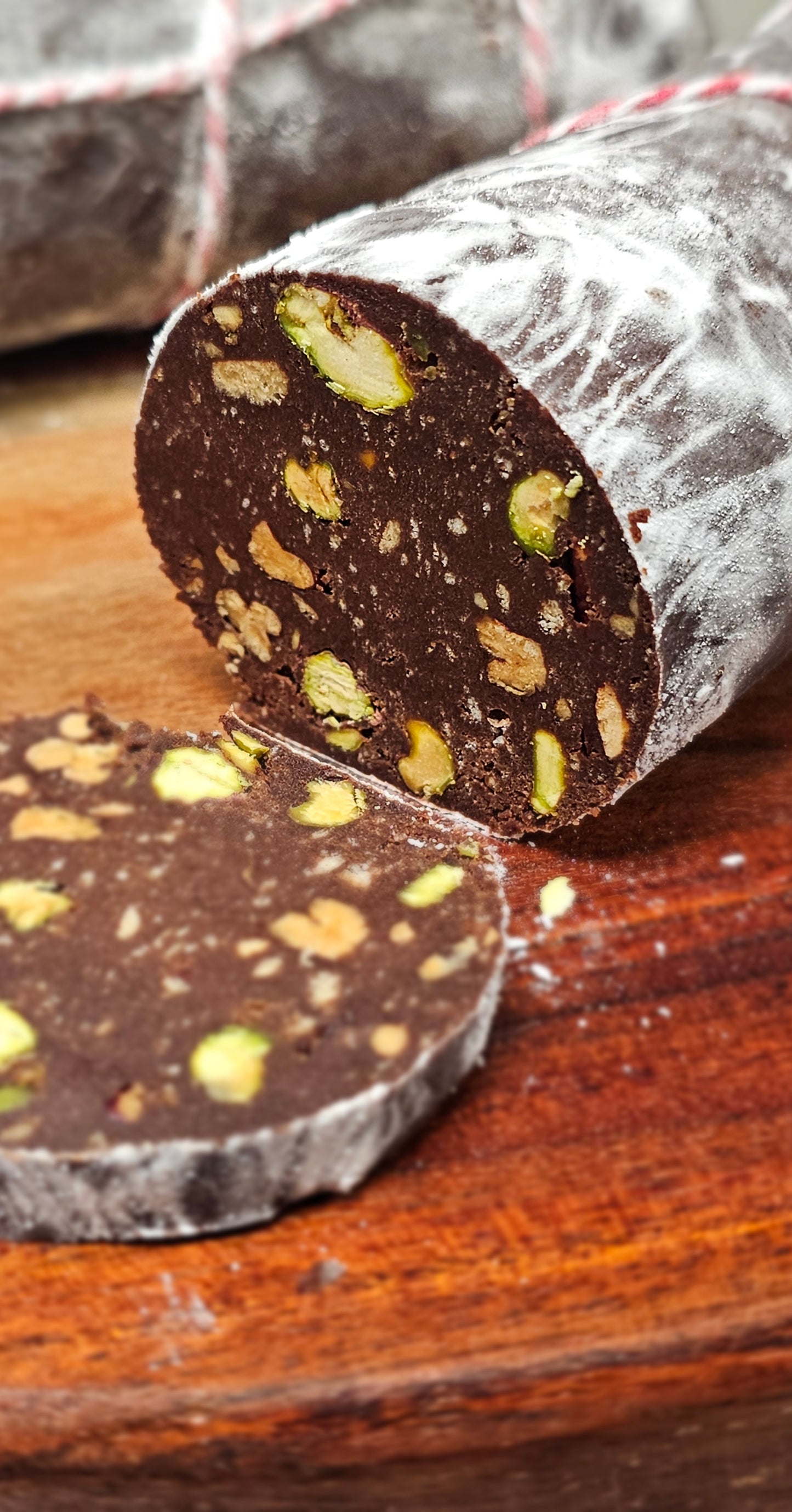 Close-up of a sliced chocolate salami with nuts on a wooden surface.