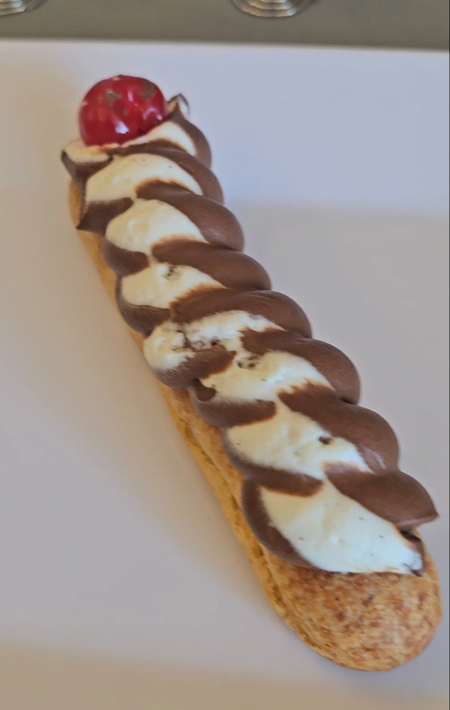 Eclair with a chocolate and vanilla cream swirl on a white plate.