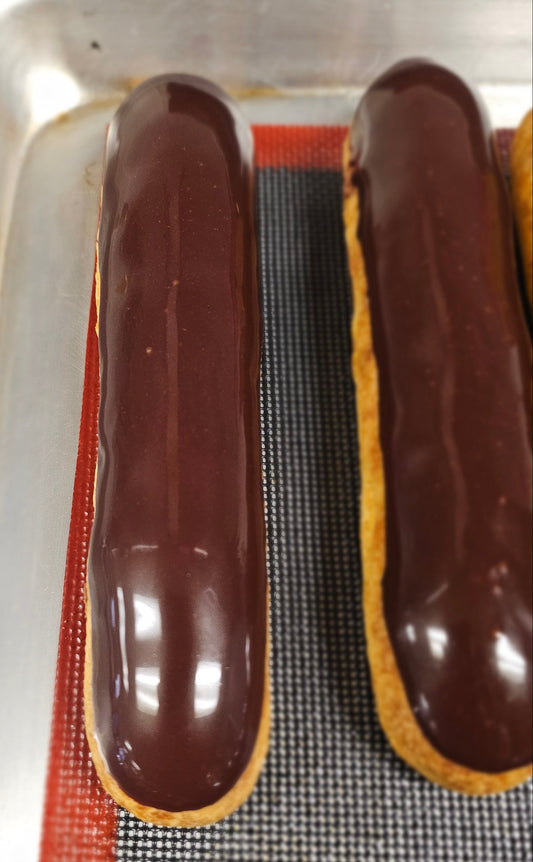 Chocolate eclairs on a baking tray with a mesh rack underneath.