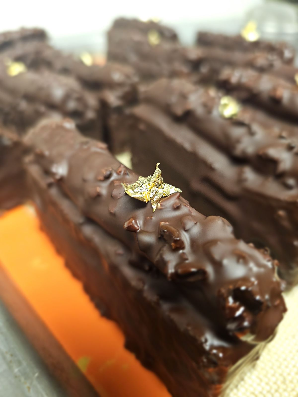 Multiple caramel travel cakes lined up, coated in chocolate and decorated with gold leaf.