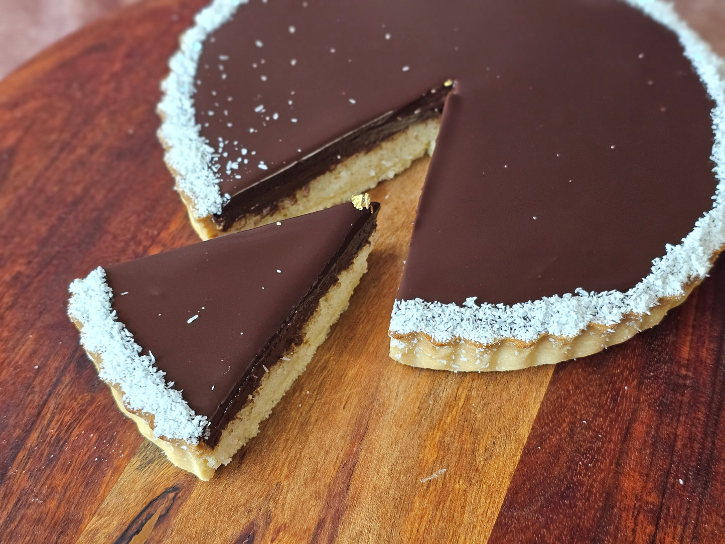 Chocolate tart with a slice removed on a wooden board