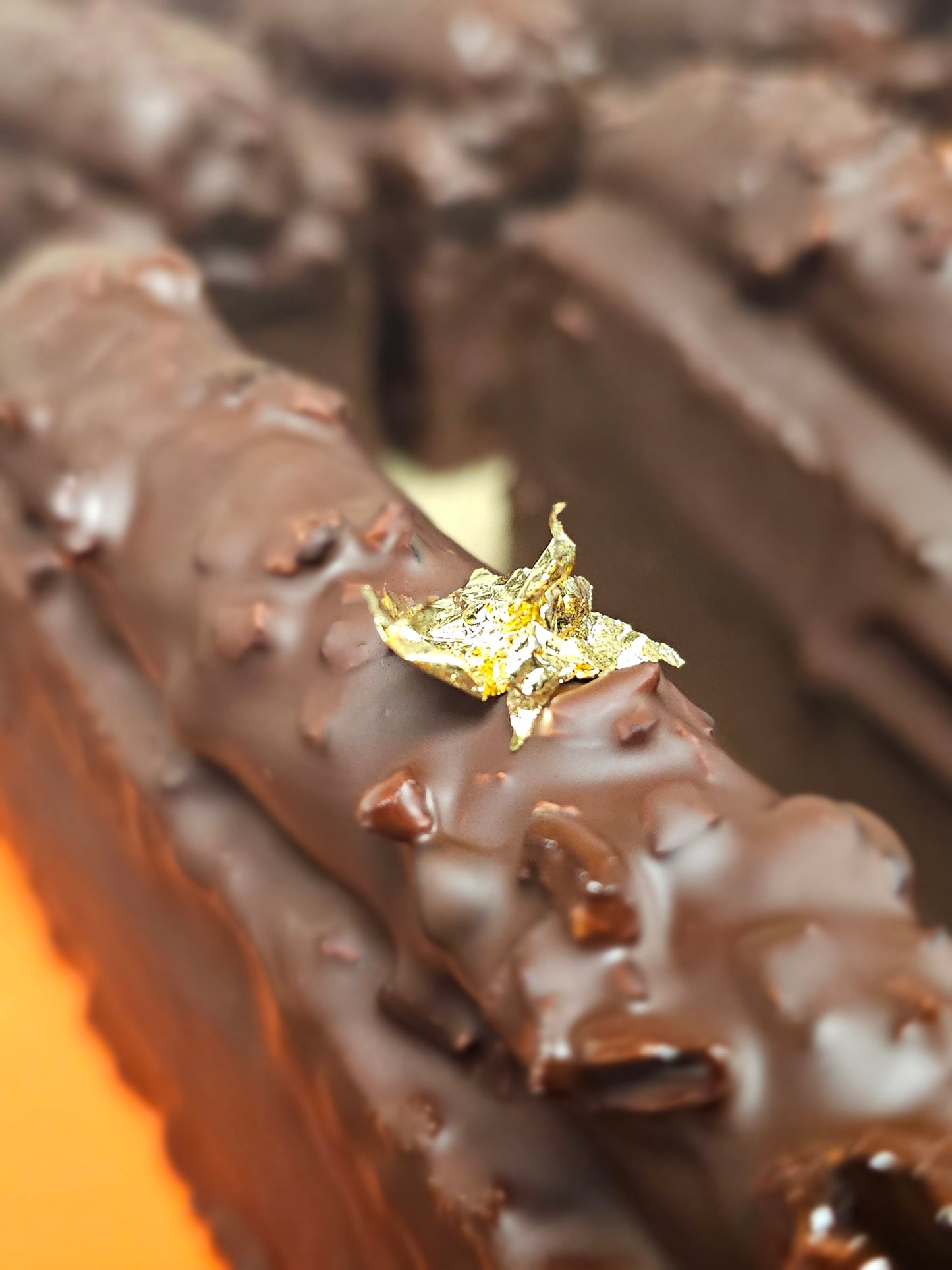 Multiple caramel travel cakes lined up, coated in chocolate and decorated with gold leaf. Close up on the gold leaf.