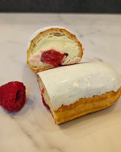 A sliced vanilla raspberry eclairs on a light background, garnished with a raspberry on the side.