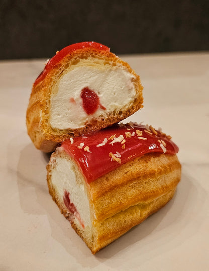 A photo showing a coconut raspberry eclairs with a glossy red icing and a raspberry on top, sliced in half.