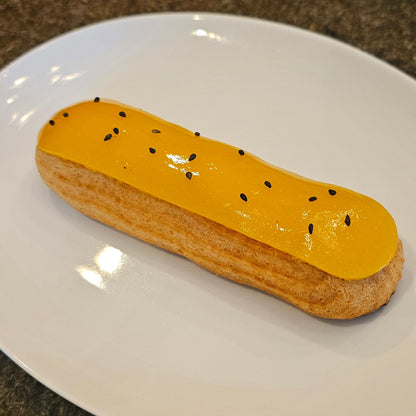 An Éclair with a yellow glaze and black seeds on top, served on a white plate.