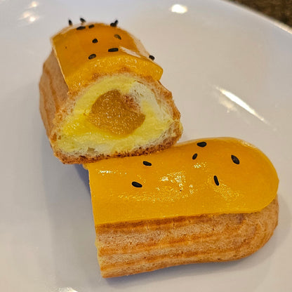 An sliced Éclair with a yellow glaze and black seeds on top, served on a white plate.