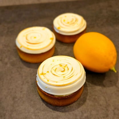 Three Lemon Poppy Seed Tartlets with a lemon next to them on a grey surface.