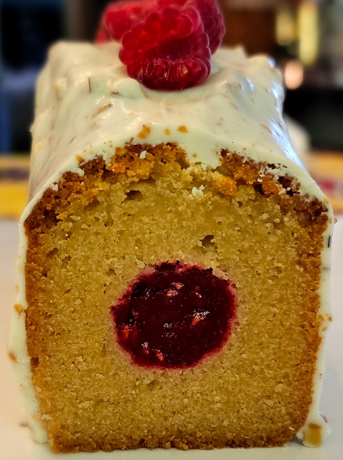 Slice of cake with raspberry filling and a raspberry on top, on a white plate.
