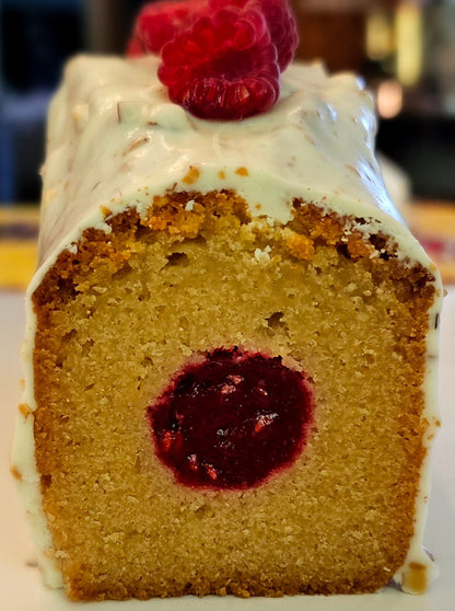 Slice of cake with raspberry filling and a raspberry on top, on a white plate.