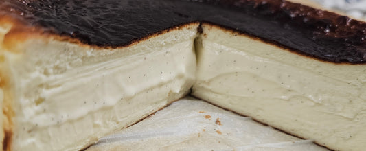 A close-up of a basque cheesecake with a dark caramelized crust and a slice cut out, resting on parchment paper.