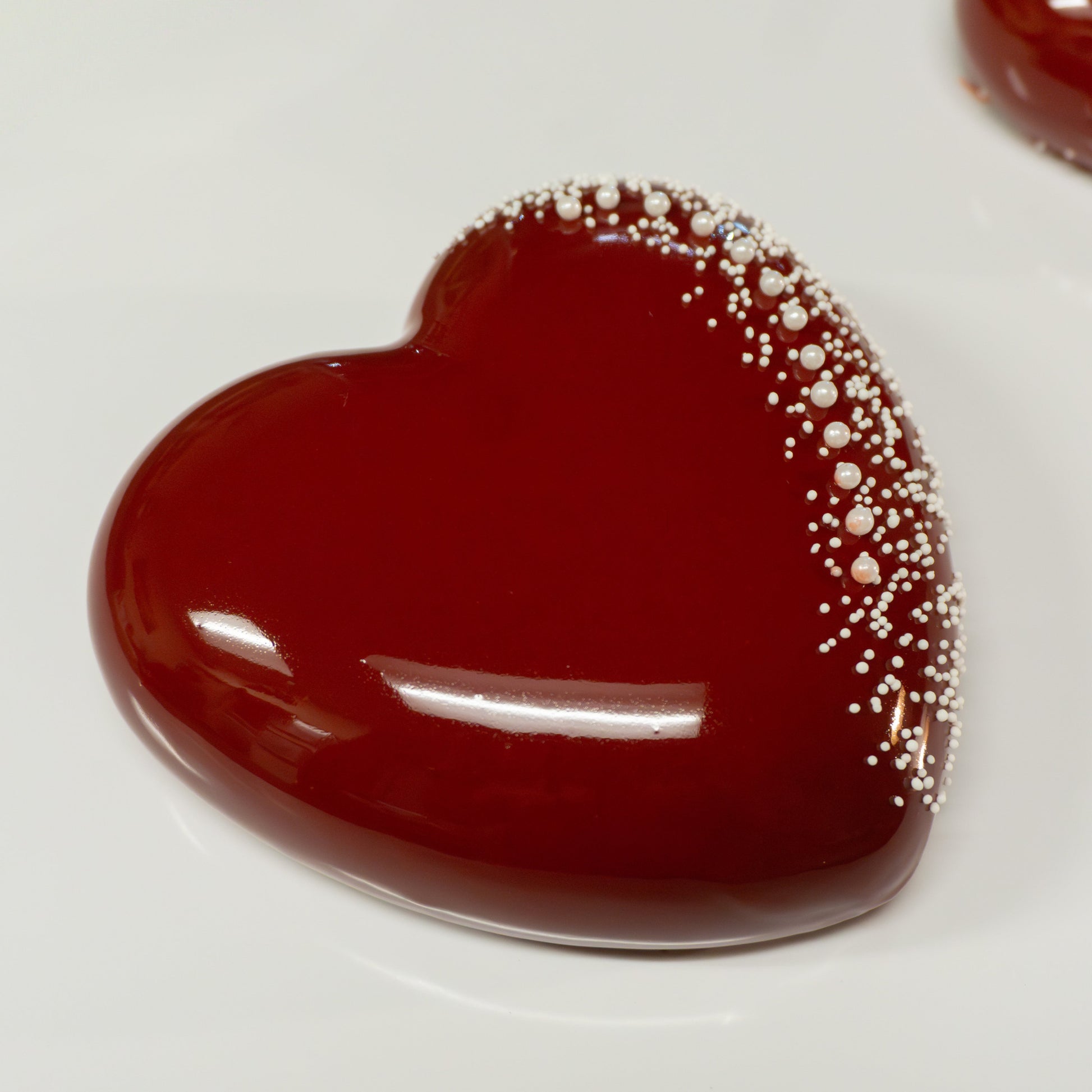 Heart shaped cake with shiny red mirror glaze accented with white earl candies.