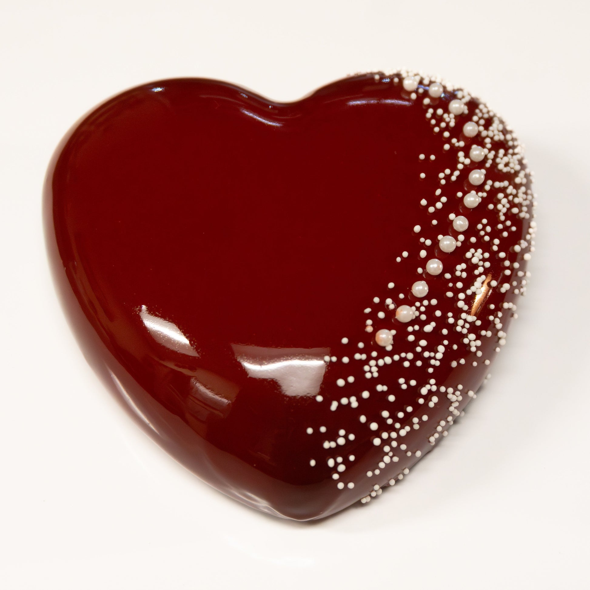 Heart shaped cake with shiny red mirror glaze accented with white earl candies.