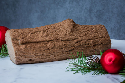 Buche de Noel mousse cake with pine decorations and red balls against a blue background 
