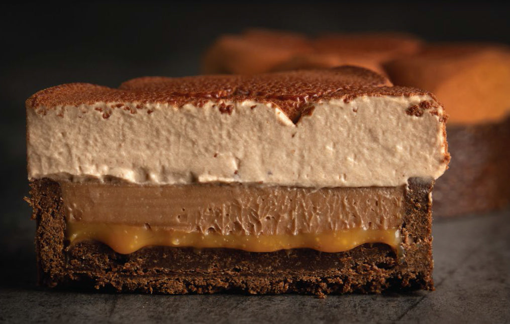 Close up of a chocolate and caramel tart sliced in half, showing the layers of cremeux, caramel and chocolate sable.