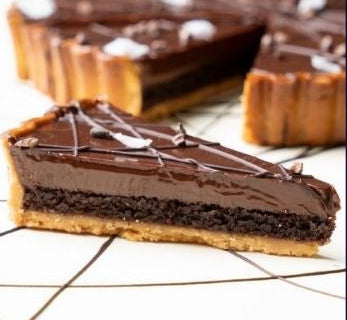 Slice of chocolate hazelnut tart on a white surface.
