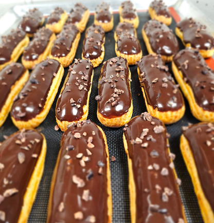 Several chocolate eclairs lined up. Each one coated in chocolate and sprinkled with cacao nibs.