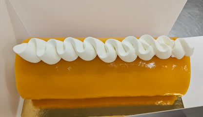Roll cake coated with orange mango glaze and white S shaped cream across the top.