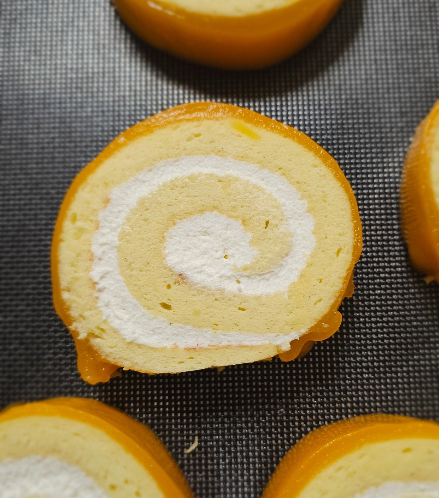 Swiss roll cake slices with white cream filling and orange glaze on a cooling rack.