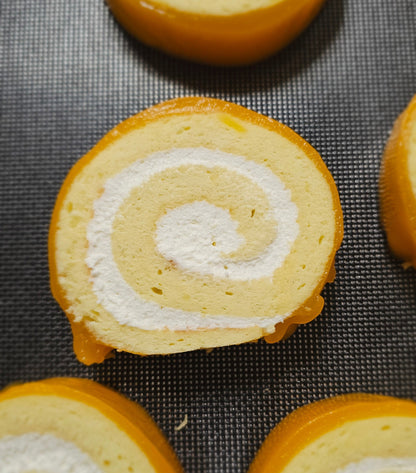 Swiss roll cake slices with white cream filling and orange glaze on a cooling rack.