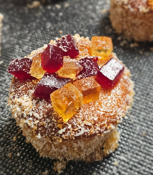 Round tea cake coated in coconut flakes and topped with cubes of raspberry and orange pate de fruit.