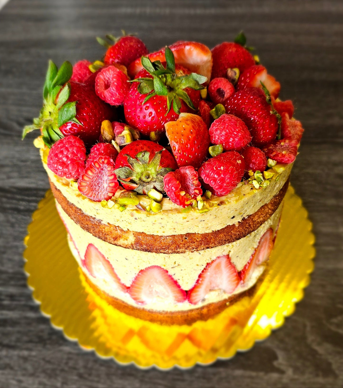 Top view Pistachio Fraisier Cake, With a ring of strawberry embedded in the side. Topped with strawberry and raspberry.
