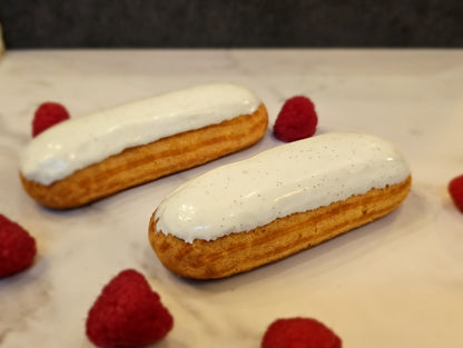 Two vanilla raspberry eclairs on a light background, garnished with white cream and raspberries on the side.