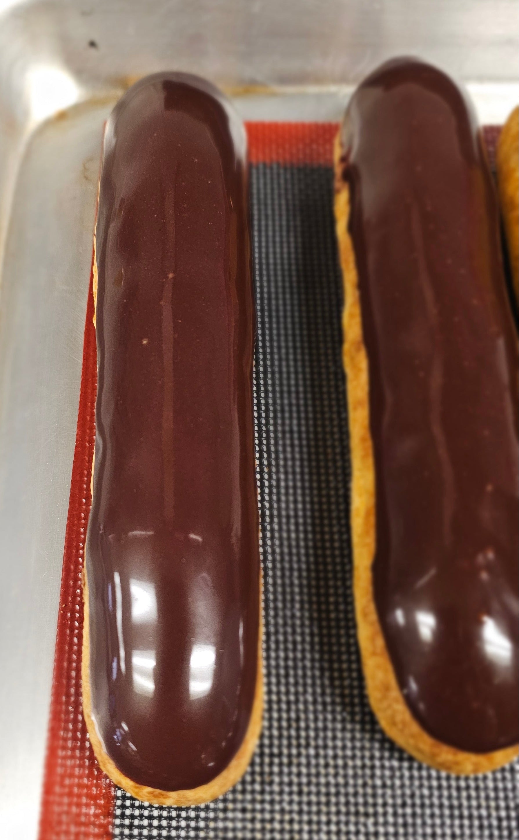 Chocolate eclairs on a baking tray with a mesh rack underneath.