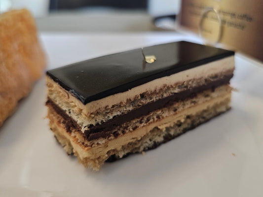 Layered opera cake dessert with chocolate, buttercream, and cake layers on a white surface.