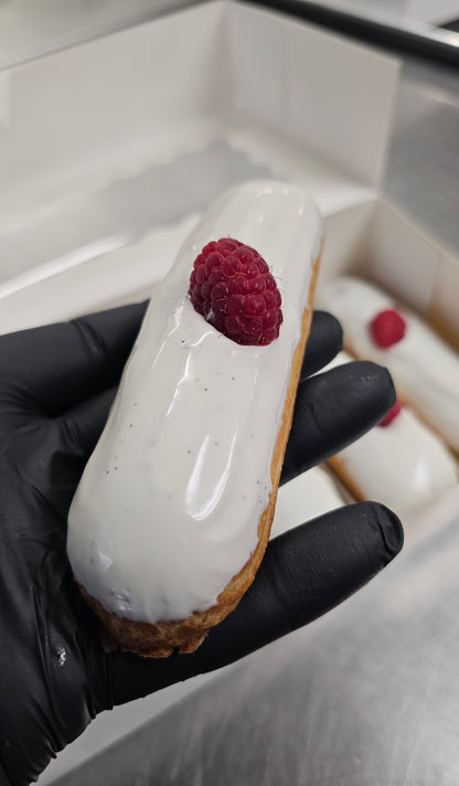 Eclair with white icing and raspberry filling held by a gloved hand.