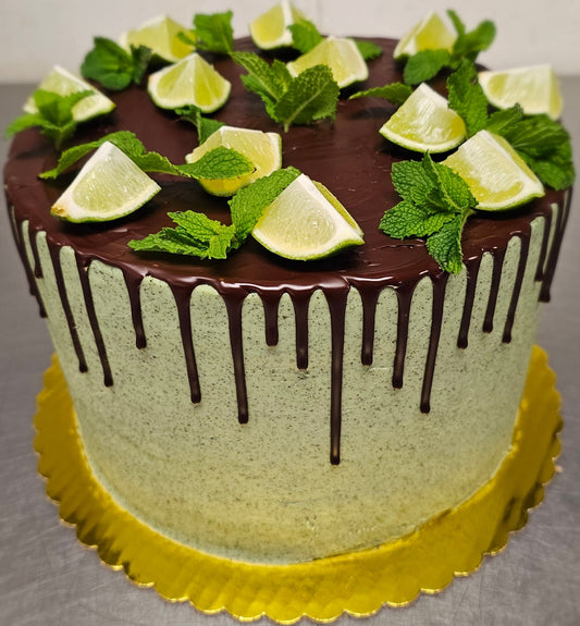 Tall mint green frosted cake topped with chocolate drips, lime wedges and fresh mint leaves.