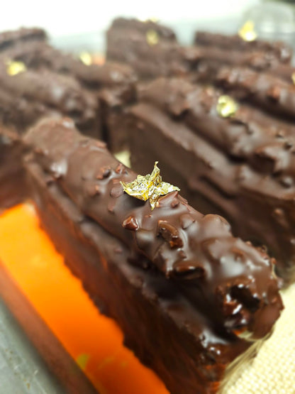 Multiple caramel travel cakes lined up, coated in chocolate and decorated with gold leaf.