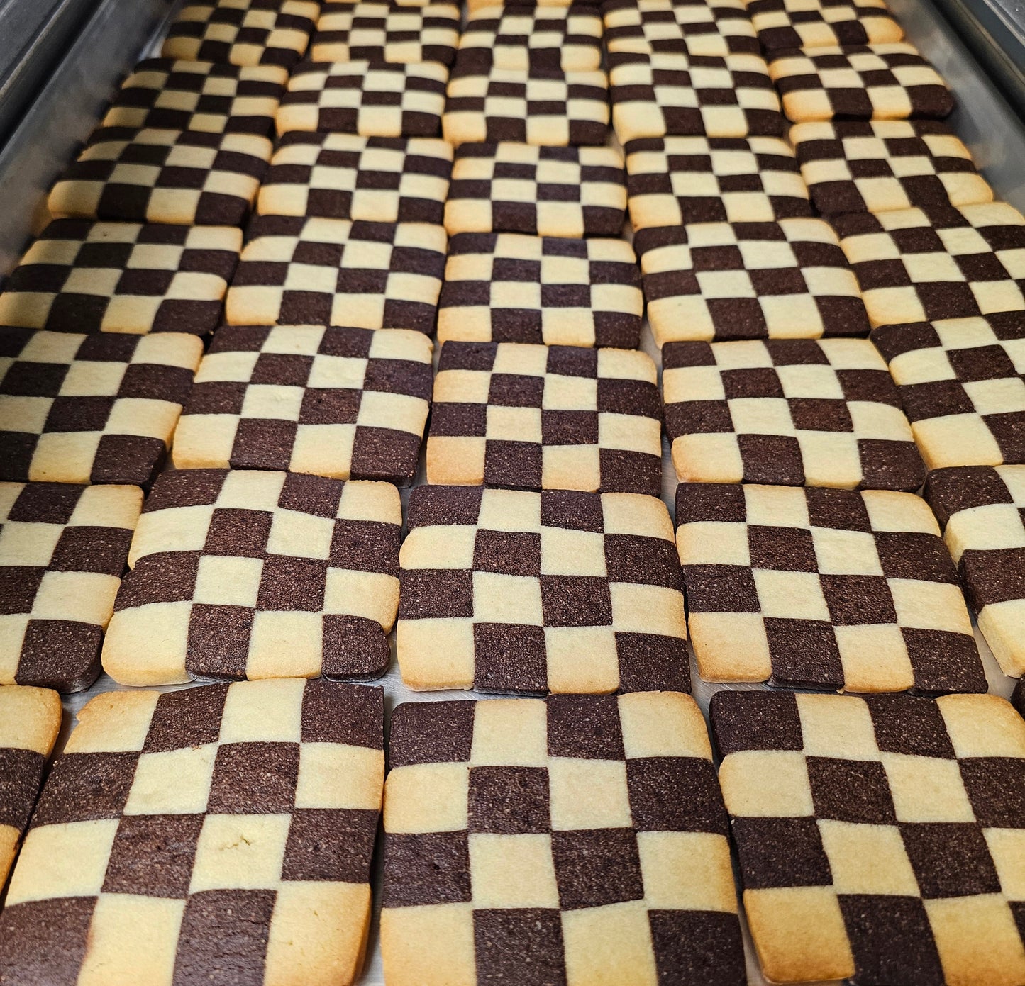Checkered pattern of brown and beige shortbread cookies in a metal tray.