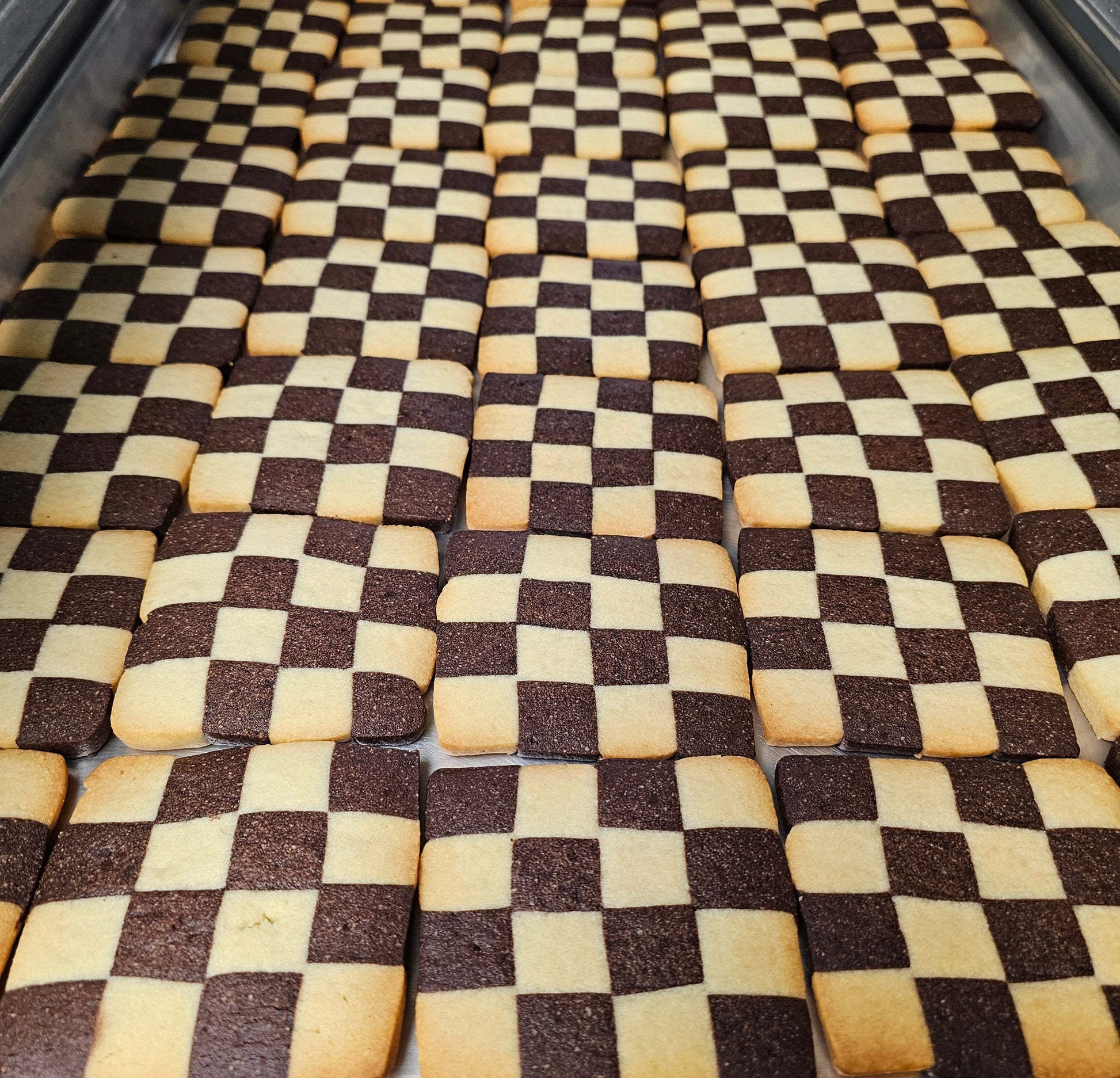 Checkered pattern of brown and beige shortbread cookies in a metal tray.