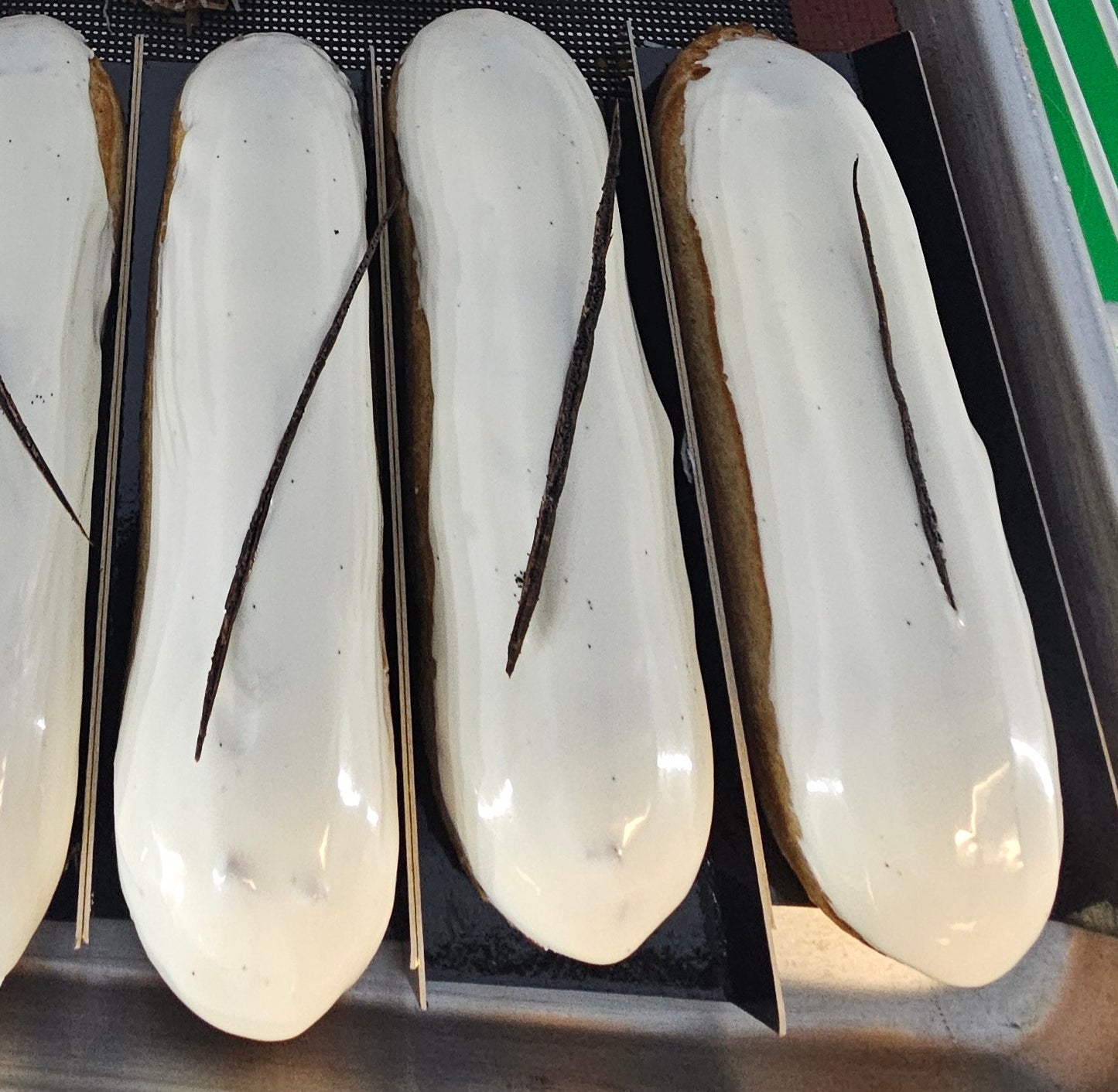 Three vanilla eclairs with white icing and decorated with a thin slice of vanilla bean.