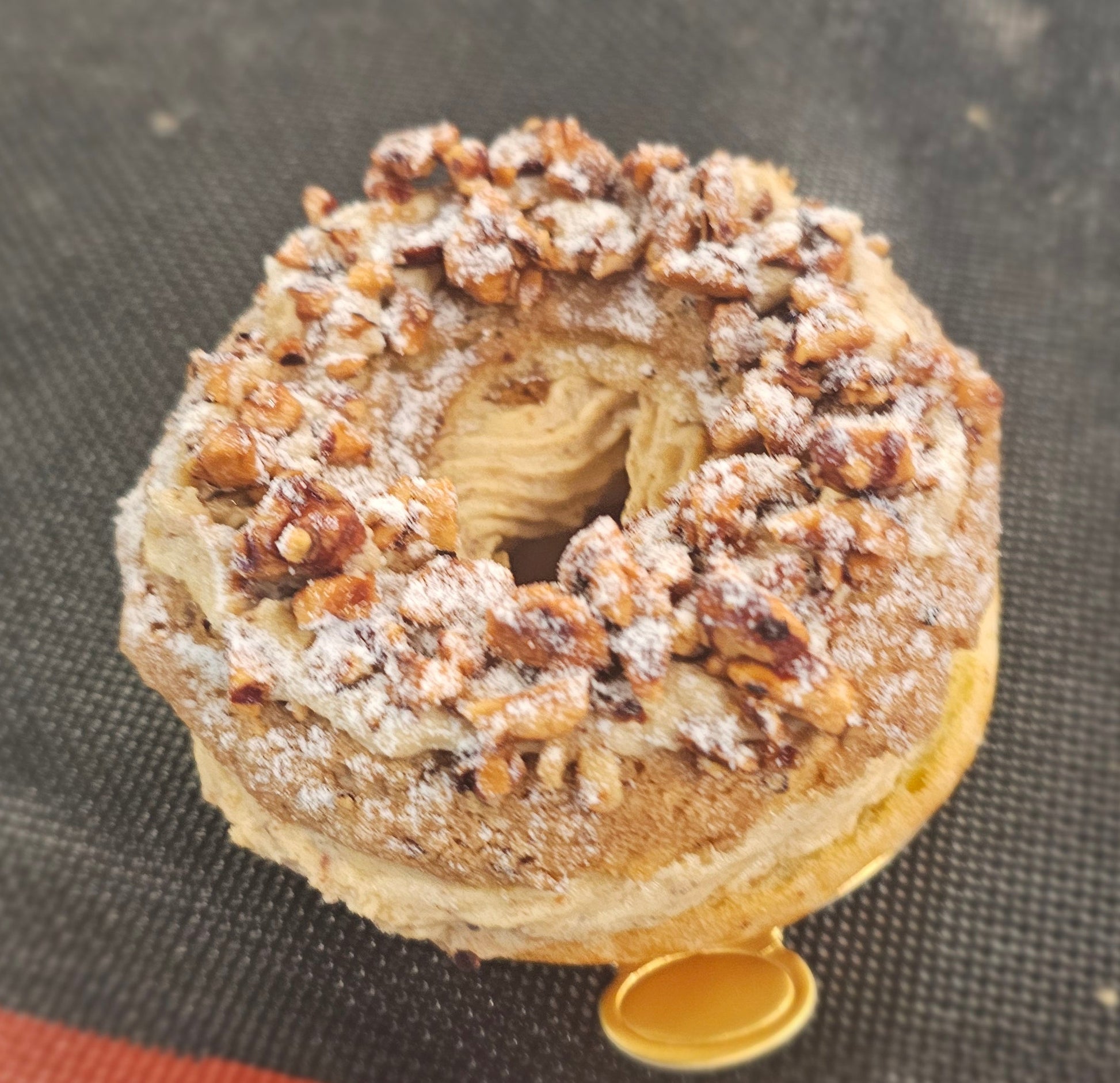 paris brest with powdered sugar and hazelnuts on a black surface