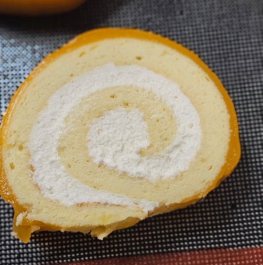 Close-up of a sliced roll cake with white cream filling on a checkered surface.