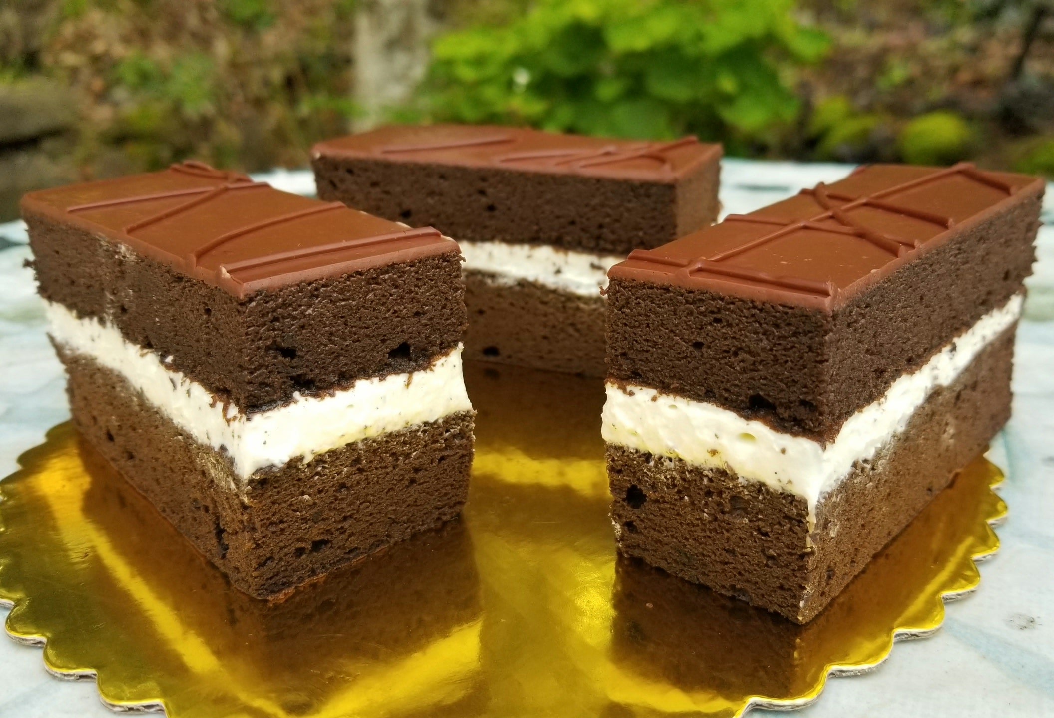Chocolate layered cakes with white cream filling  on a gold tray with a blurred natural background.