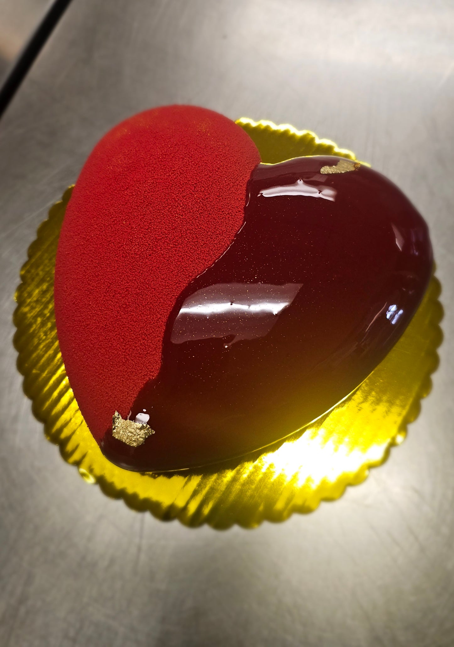Heart shaped cake with half shiny red mirror glaze and half velour coating, accented with white pearl candies.