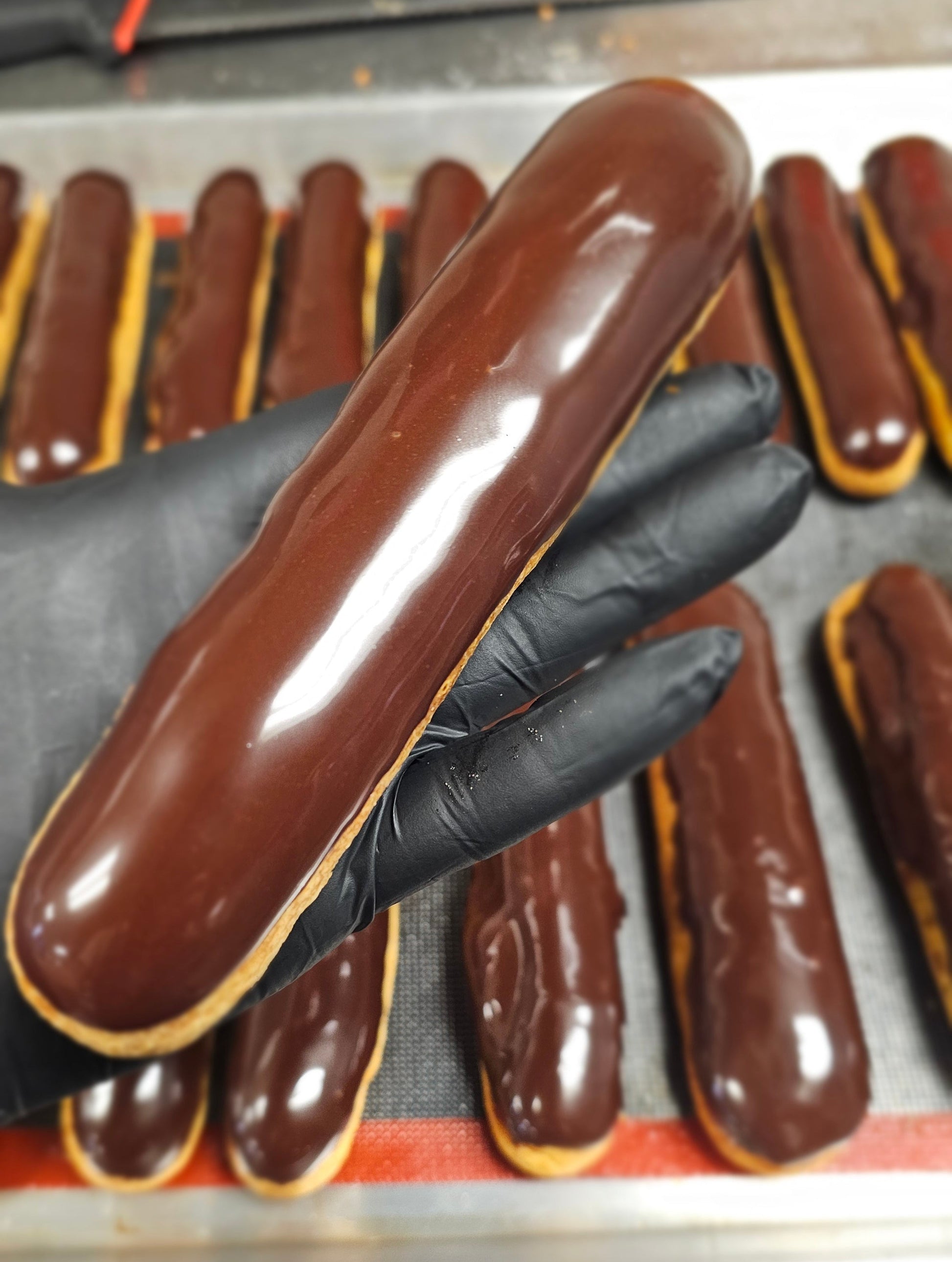 Chocolate eclairs being prepared with a gloved hand in a kitchen setting
