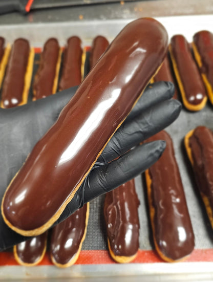Chocolate eclairs being prepared with a gloved hand in a kitchen setting