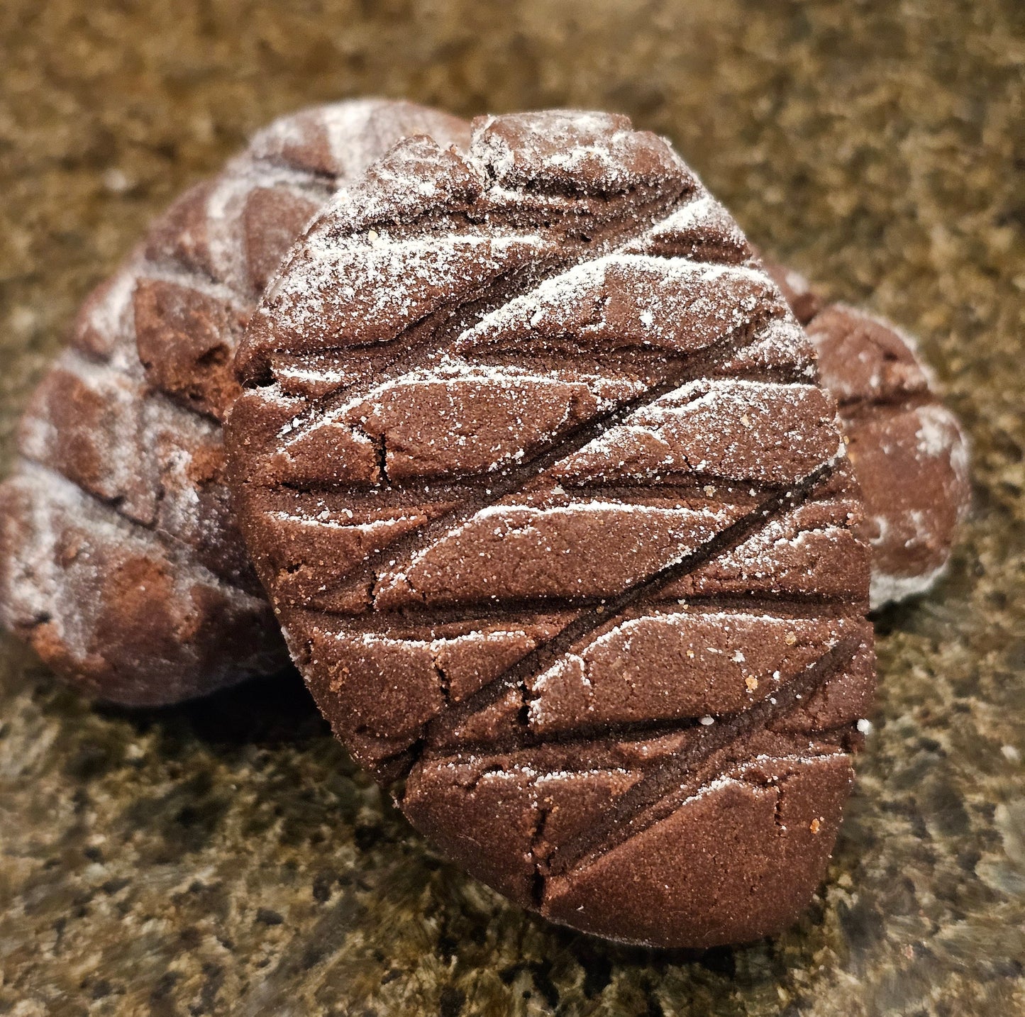 Pine cone shaped chocolate cookies dusted with sugar on a stone surface