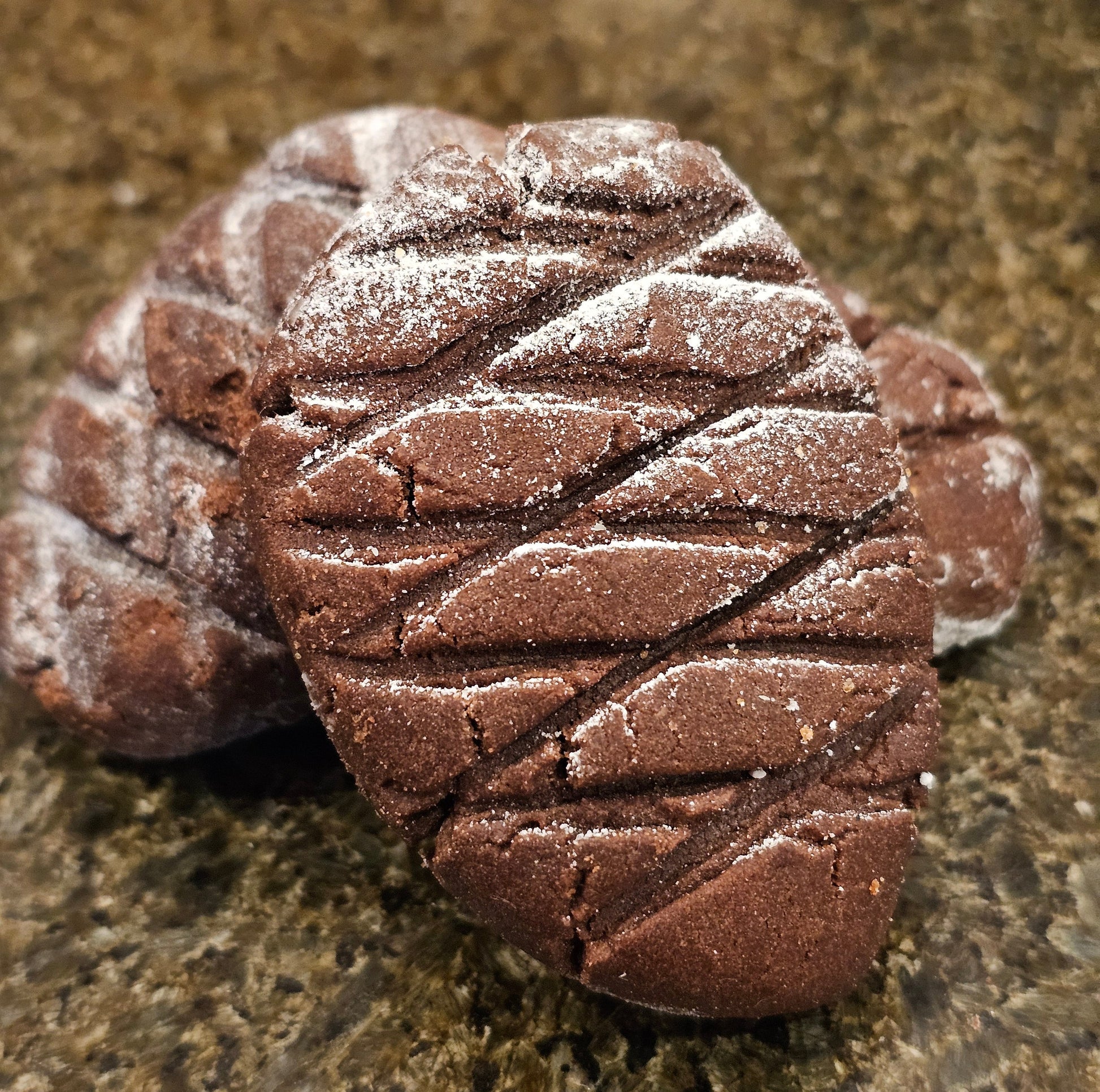 Pine cone shaped chocolate cookies dusted with sugar on a stone surface