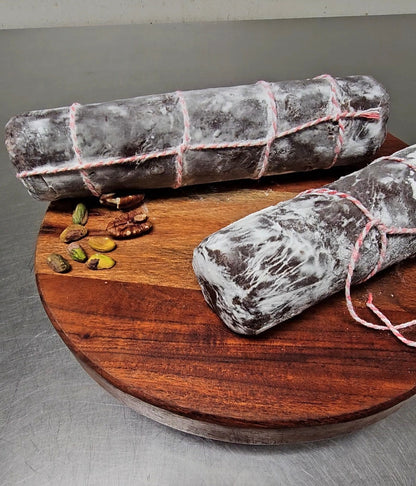 Two chocolate salamis on a wooden board with some nuts.