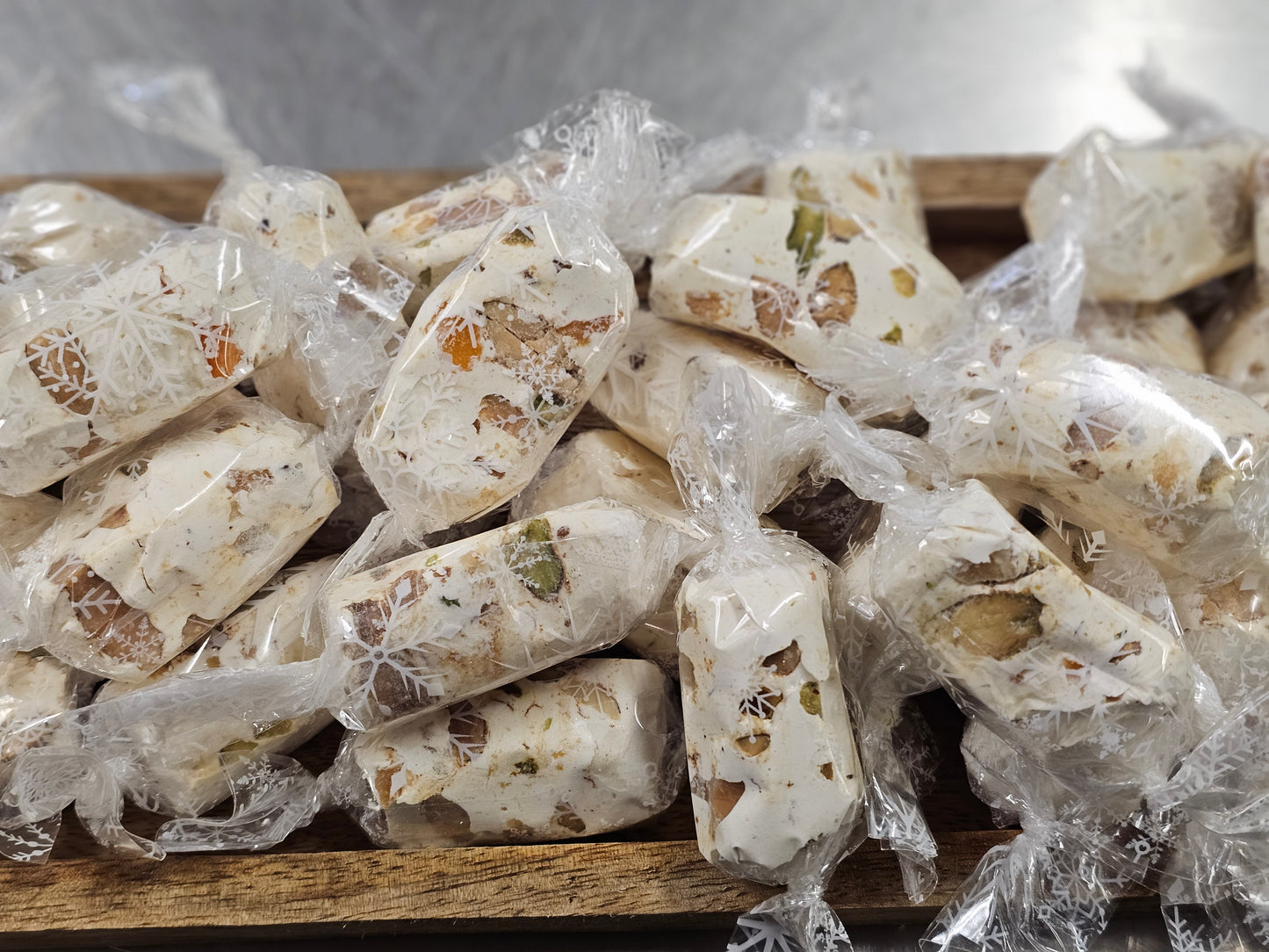 Nougat pieces wrapped in clear plastic on a wooden board with a white background